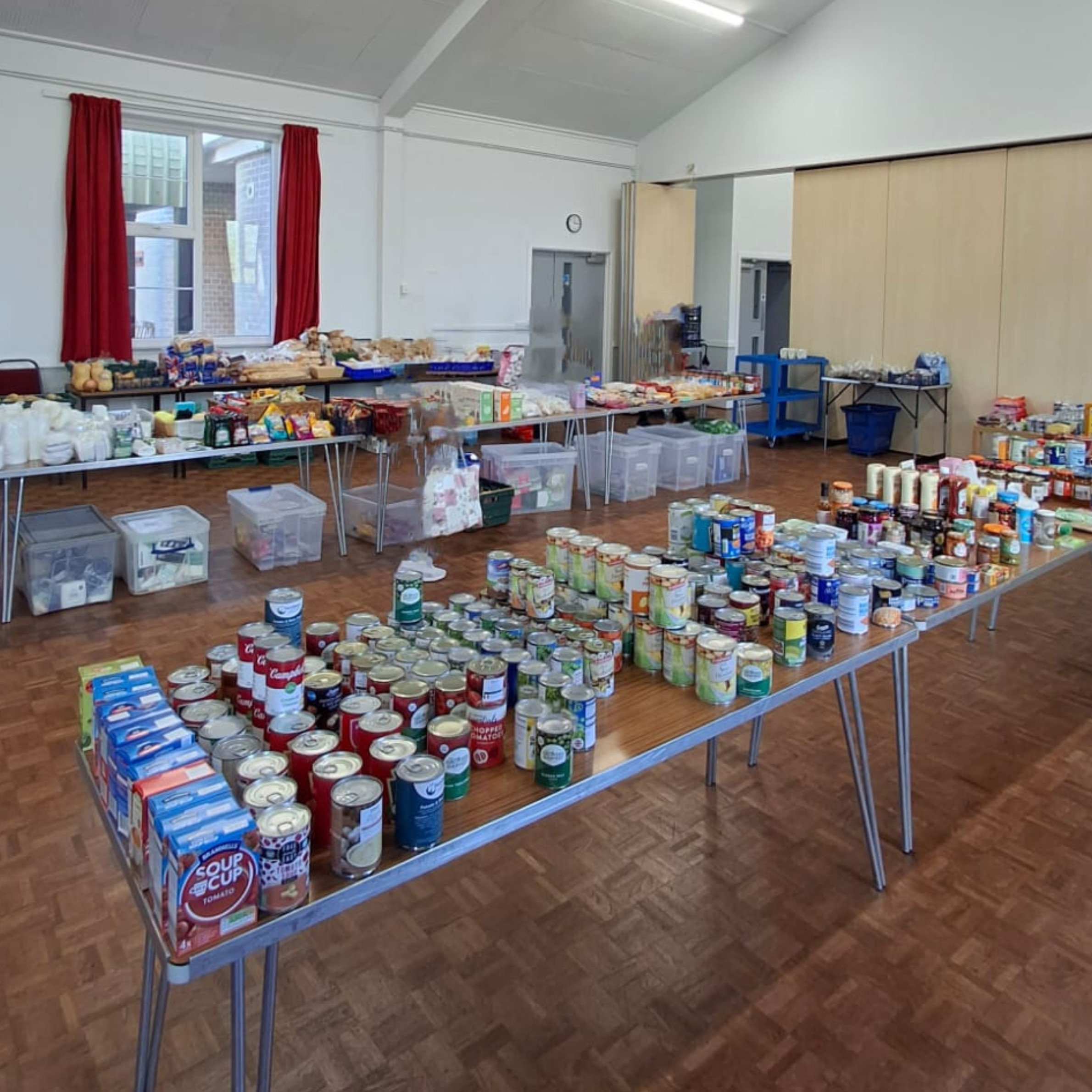 The image depicts the Turlin Moor food store set up in the St Gabrials Church hall. Mulitple tables are set up with lots of food items apon them.